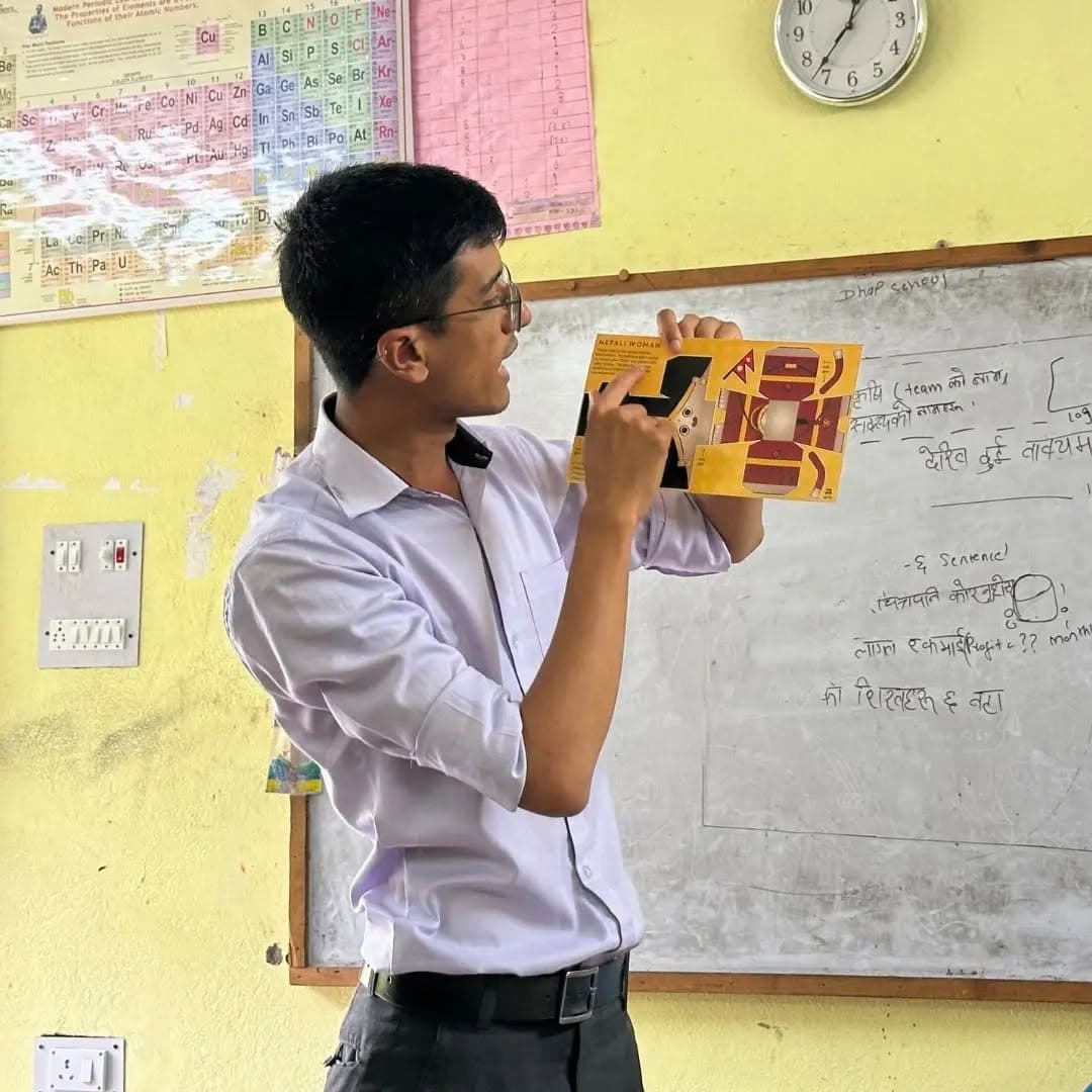 A student presenting a printed cut-out model to the class in front of a whiteboard